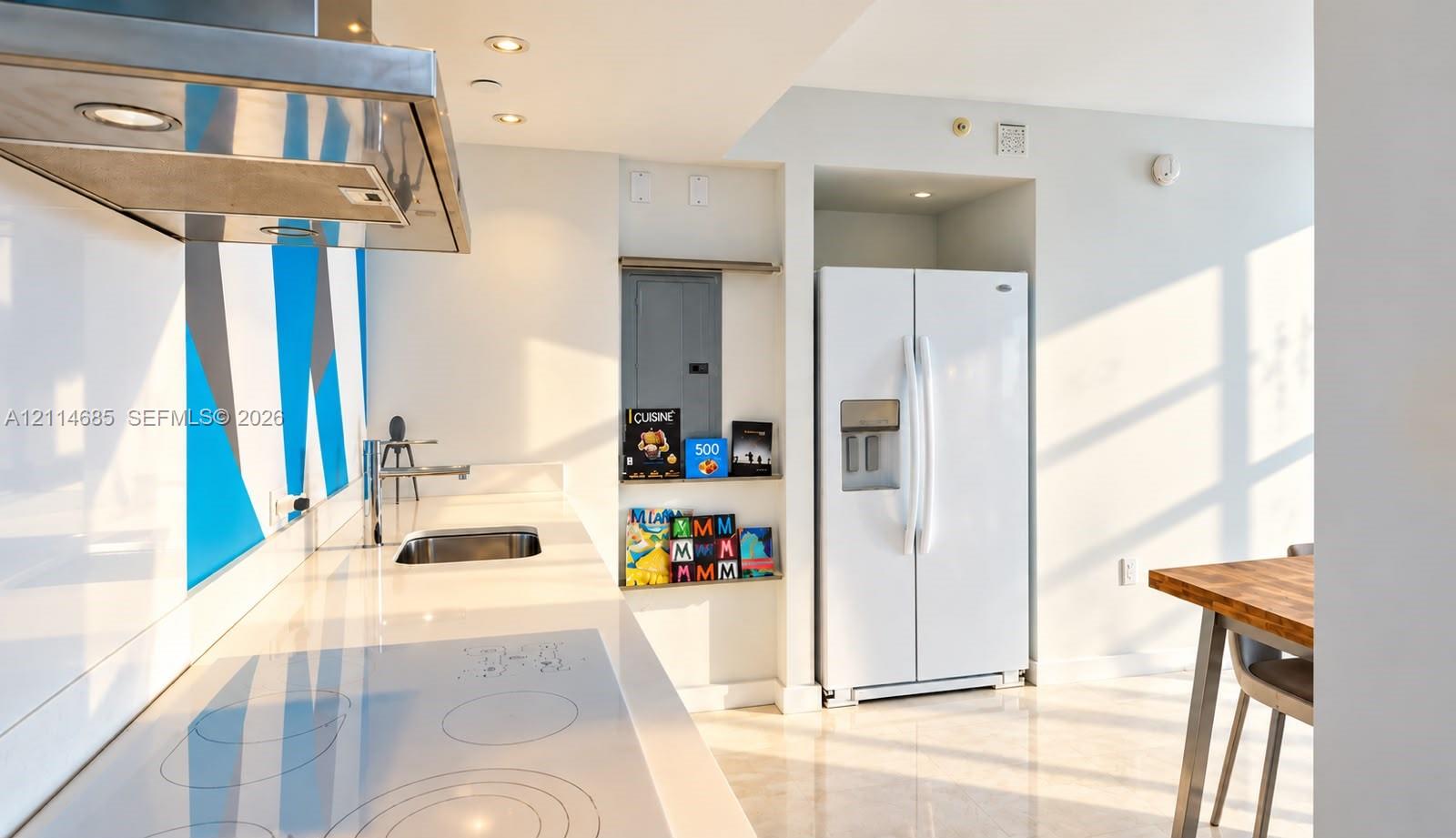 Kitchen featuring a smooth-top electric cooktop, stainless steel range hood, stone-finish countertops, integrated sink, and white side-by-side refrigerator