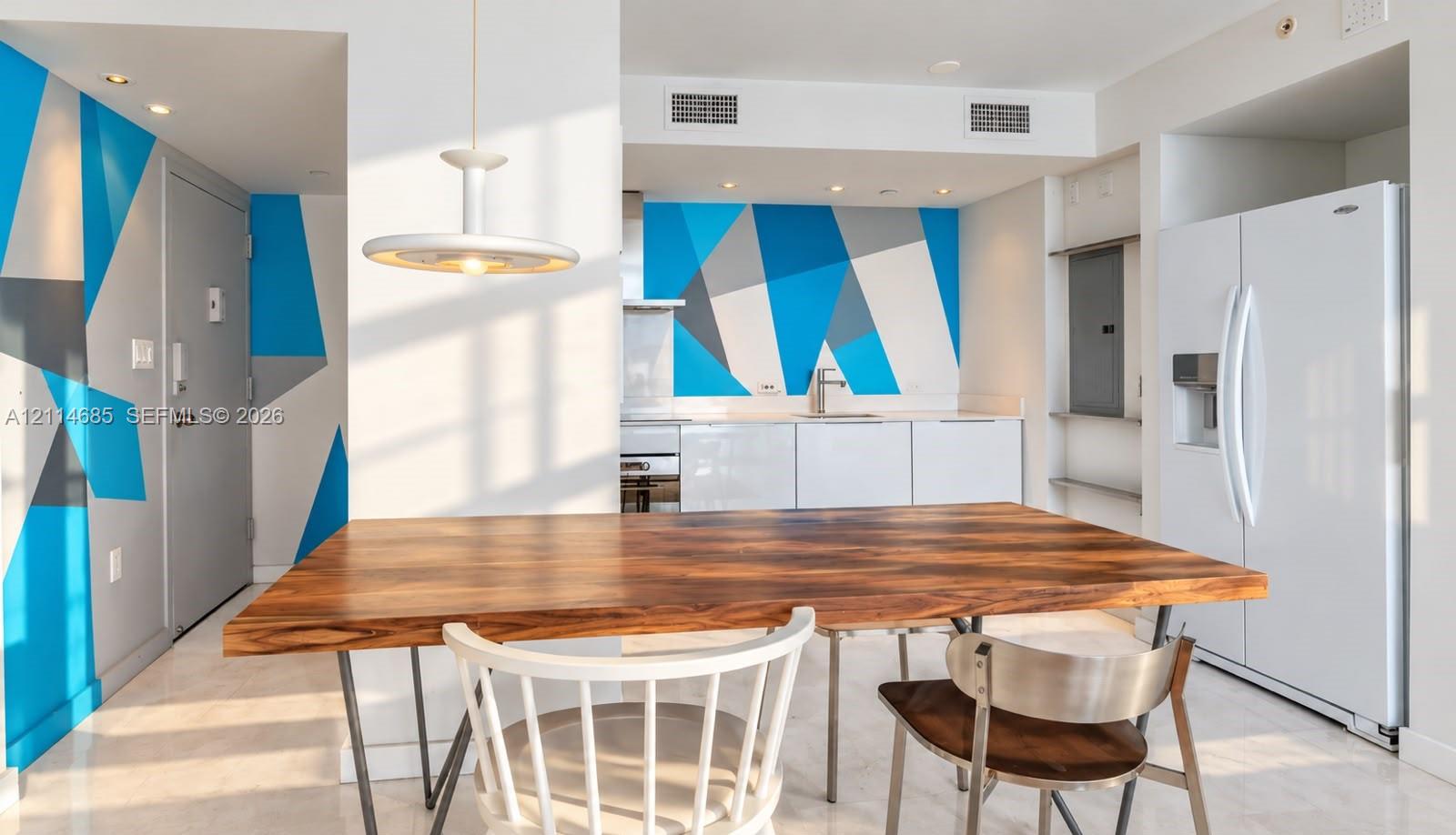 Kitchen featuring minimalist white cabinetry, a full-size refrigerator, a geometric wall mural, and a pendant light fixture
