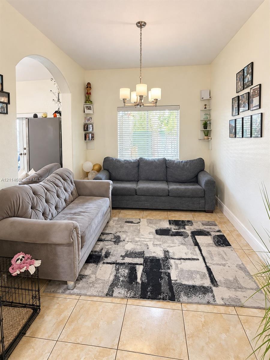 Ceramic tile flooring, arched entryway, four-light brushed-nickel chandelier, and wall-mounted shelving units