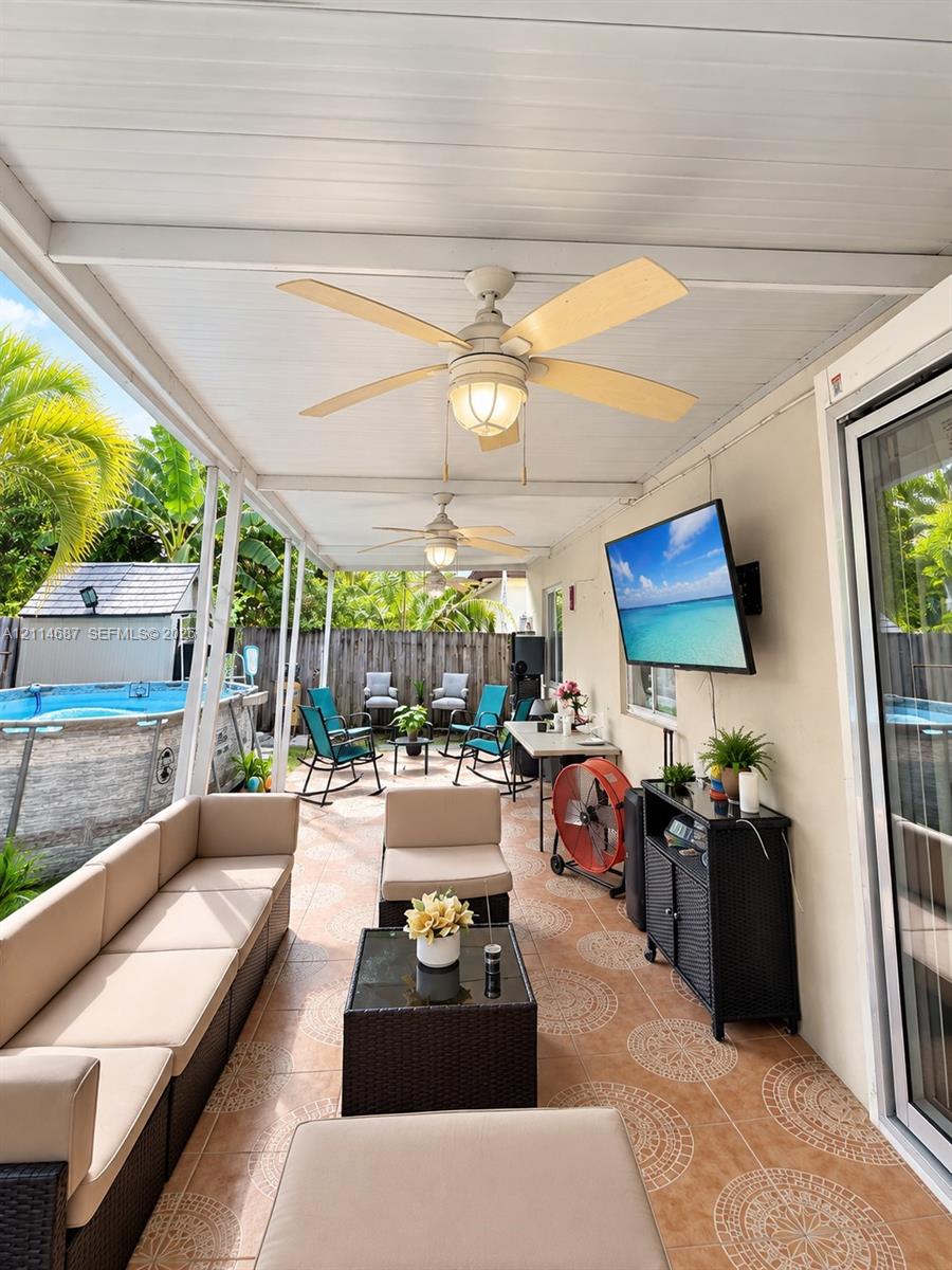 Covered patio featuring patterned tile flooring, dual overhead ceiling fans with integrated lighting, and a wall-mounted flat-screen television mount