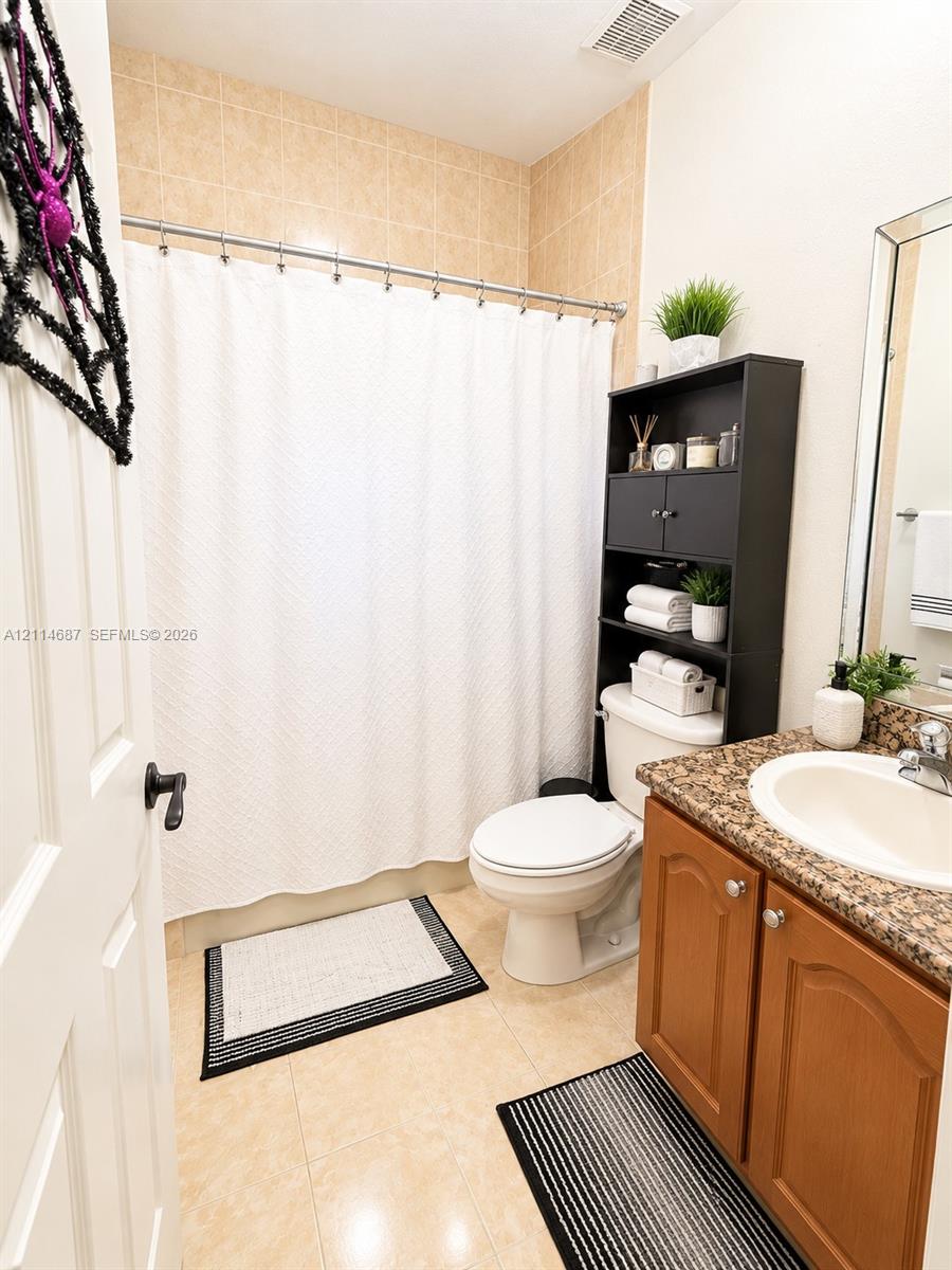 Full bathroom featuring tile flooring, a tub-shower combination with tiled surround, and a wood vanity with a stone-finish countertop and integrated sink