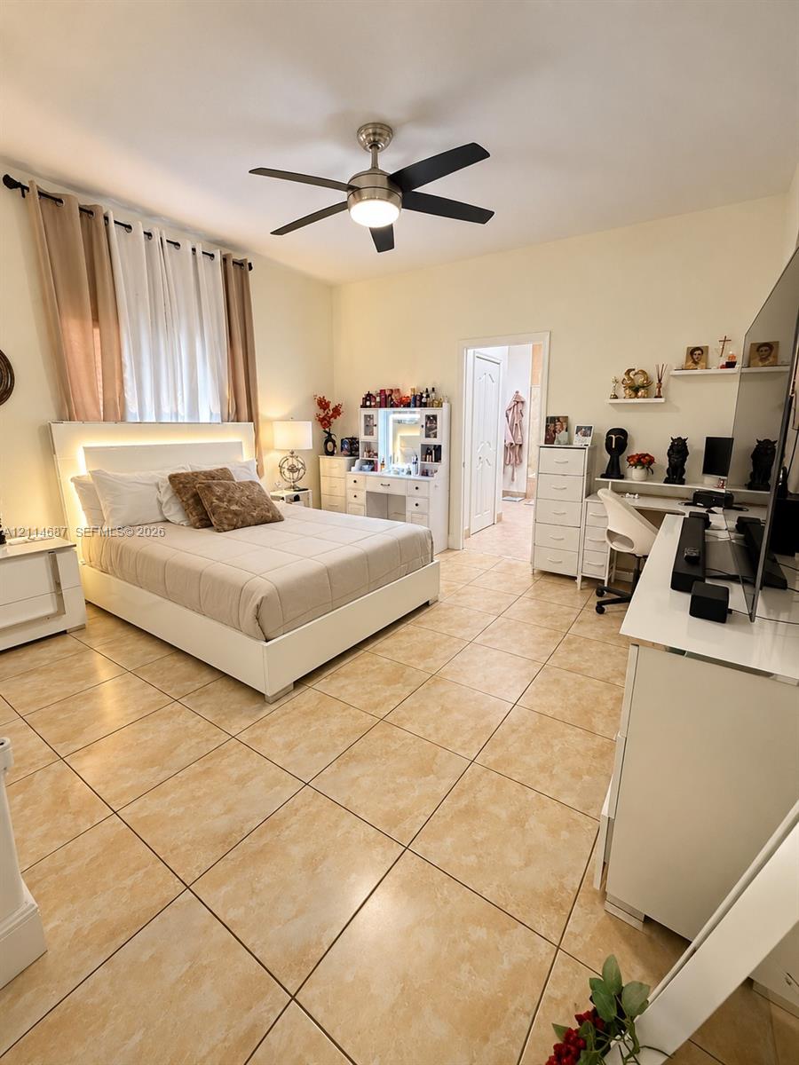 Room featuring large-format neutral tile flooring, multi-blade ceiling fan with integrated lighting, and high ceilings