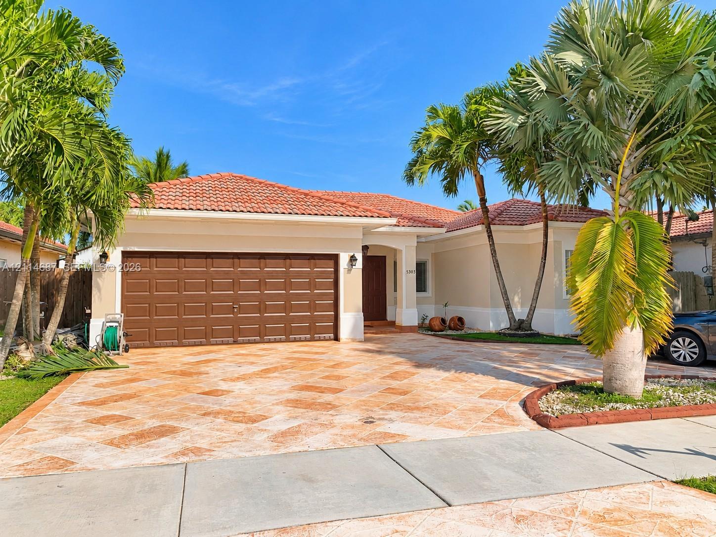 Stucco exterior featuring a terracotta tile roof, paver driveway, multi-car garage, and mature palm landscaping Stucco exterior featuring a terracotta tile roof, paver driveway, multi-car garage, and mature palm landscaping