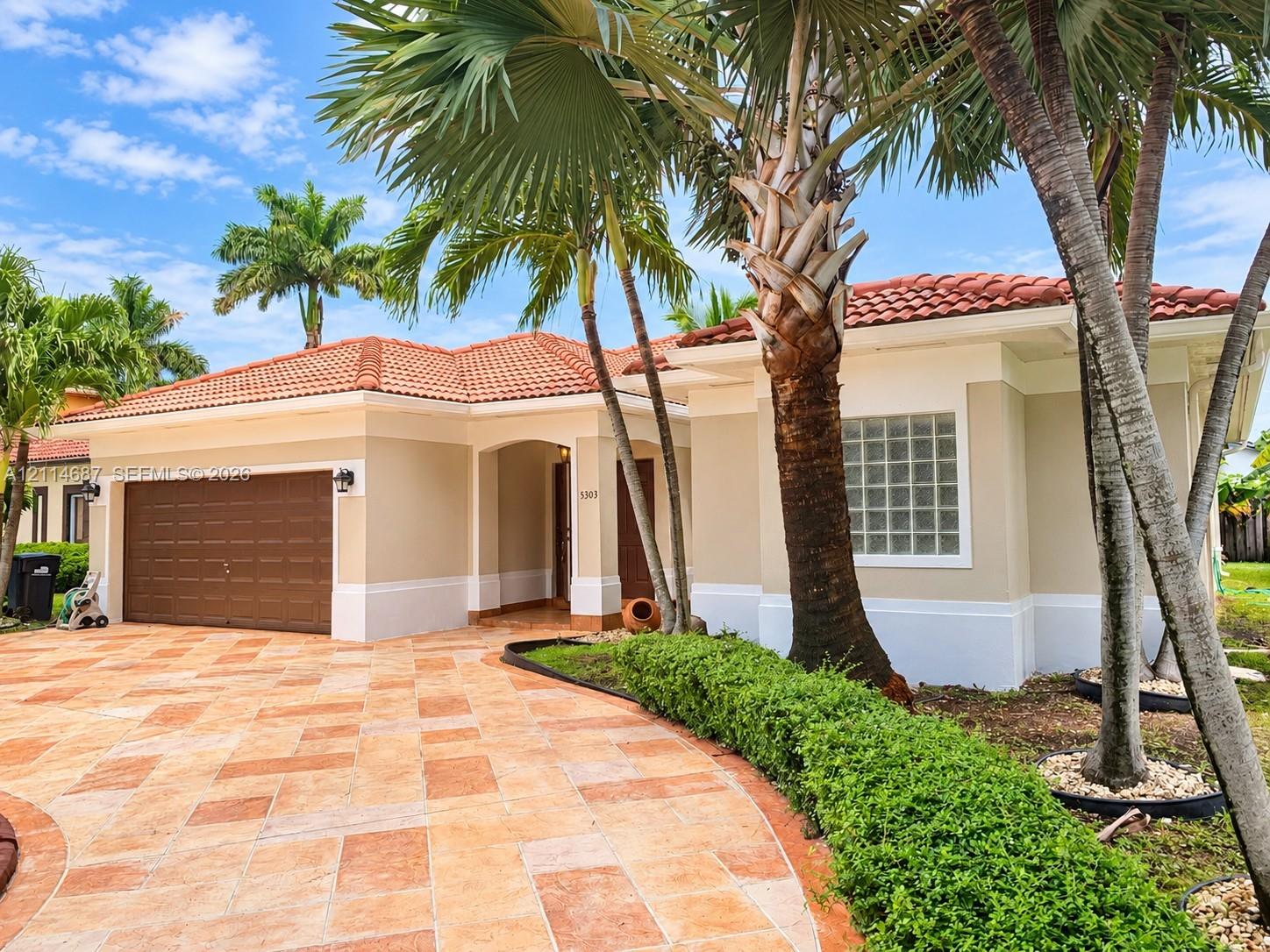 Exterior featuring a tile roof, stucco finish, paver driveway, glass block window, and mature palm trees Exterior featuring a tile roof, stucco finish, paver driveway, glass block window, and mature palm trees
