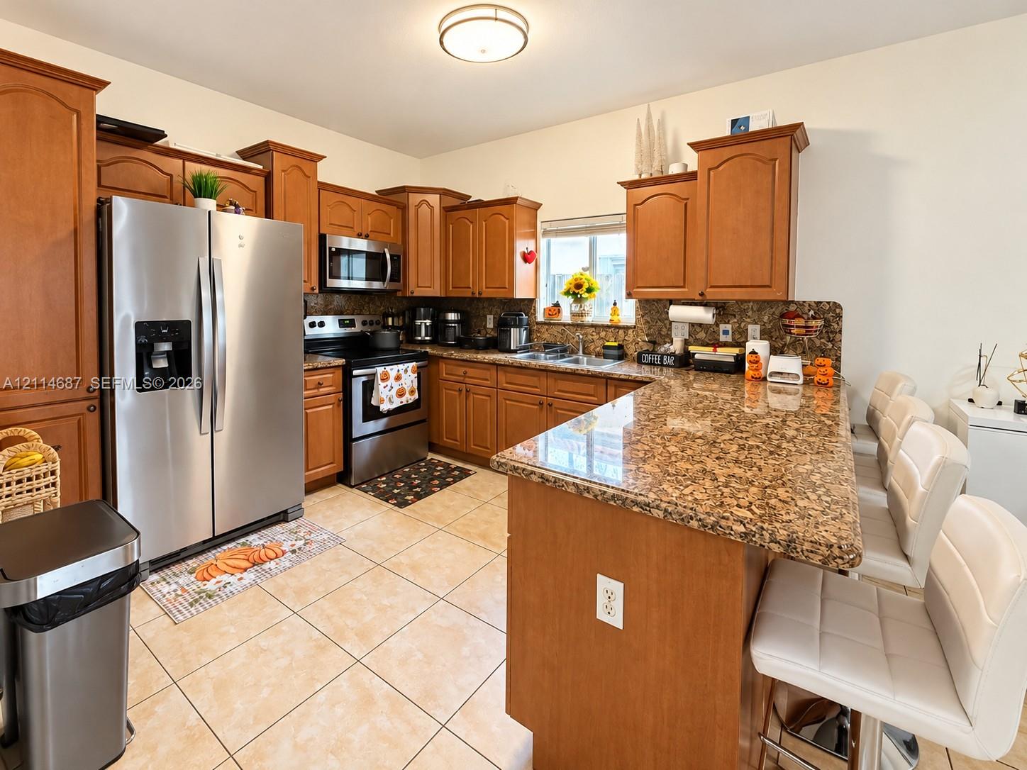 Kitchen featuring medium-toned wood cabinetry, stone countertops, stainless steel appliances, breakfast bar, and tile flooring