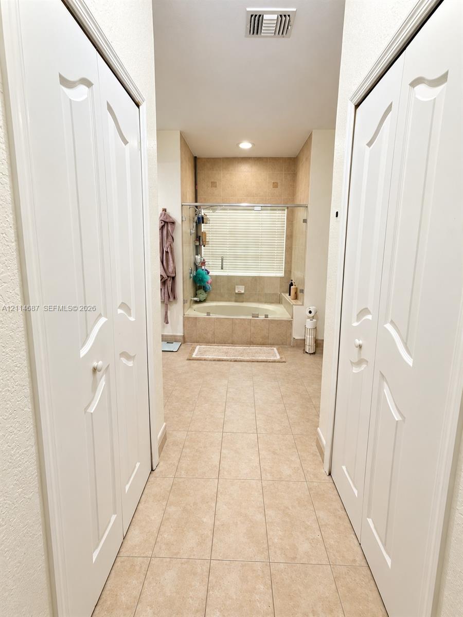 Built-in dual-panel closet doors, recessed lighting, and tile flooring, featuring a tiled soaking tub with glass enclosure