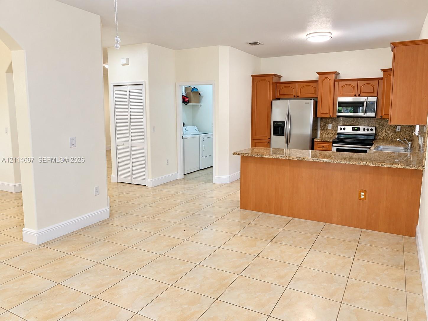 Kitchen featuring wood cabinetry, stone-finish countertops, stainless steel appliances, a breakfast bar, and tile flooring