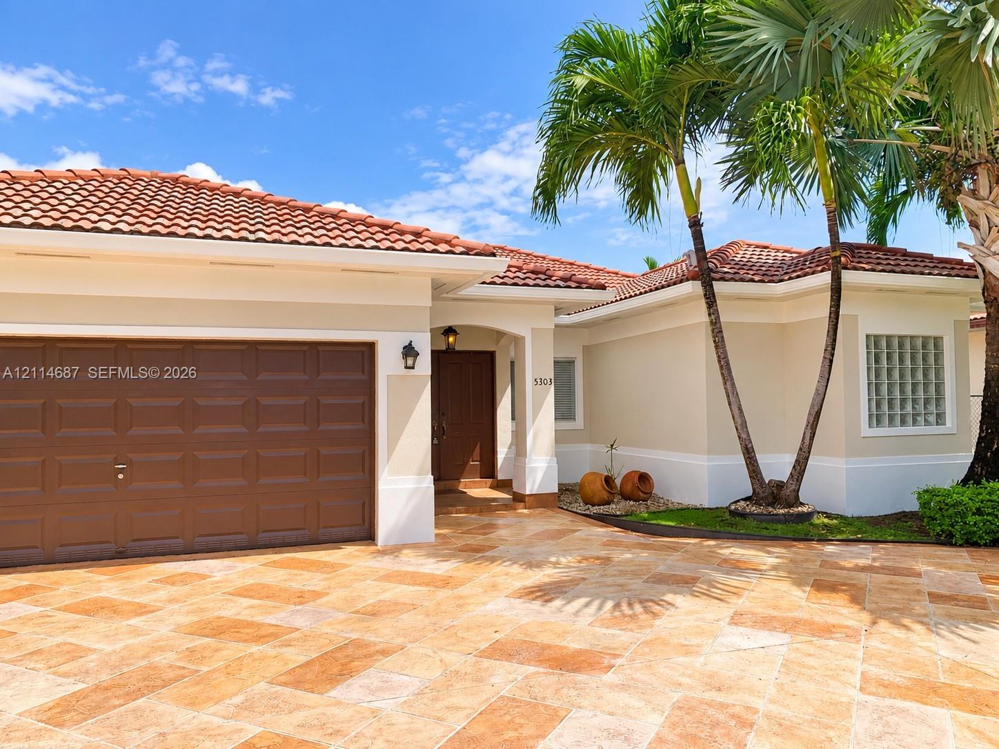 Exterior facade featuring a terracotta-tiled roof, stone-paver driveway, single-panel garage door, and glass block window accents