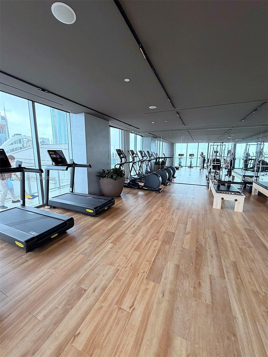 Fitness center featuring wood-finish flooring, floor-to-ceiling windows, integrated track lighting, and mirrored wall surfaces