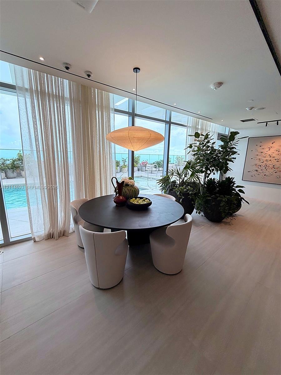 Floor-to-ceiling glass windows, recessed ceiling lighting, wood-finish flooring, and a contemporary saucer-style pendant light