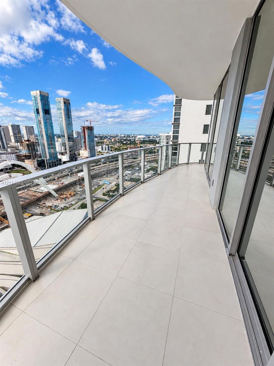 Covered wrap-around balcony featuring large-format tile flooring, a glass panel railing, and floor-to-ceiling sliding glass doors