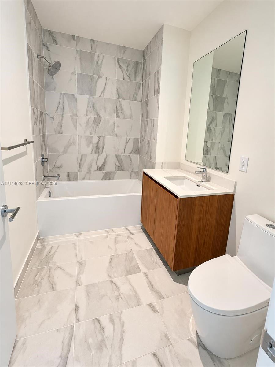 Bathroom featuring large-format tile flooring, wood-finish vanity with a rectangular sink, quartz countertop, and a tub-shower combination with tiled surround