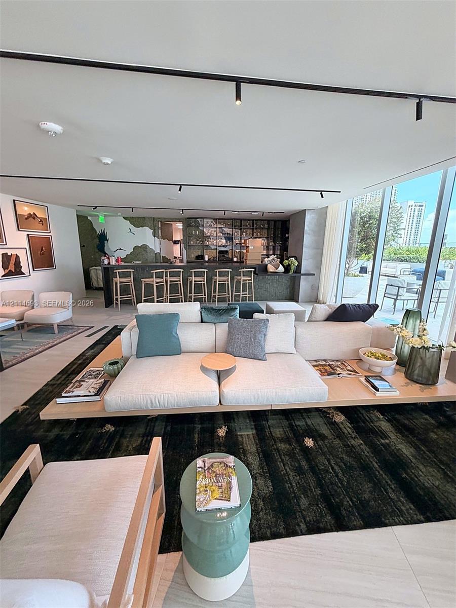 Open-concept interior featuring floor-to-ceiling glass walls, built-in bar with stone-finish surfacing, track lighting, and expansive stone-tile flooring