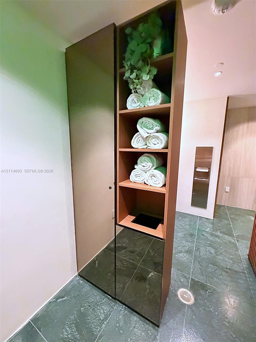 Full-height built-in cabinetry featuring open shelving and a solid-panel door, set against stone-finish floor tiling with a stainless steel wall-mounted dispenser