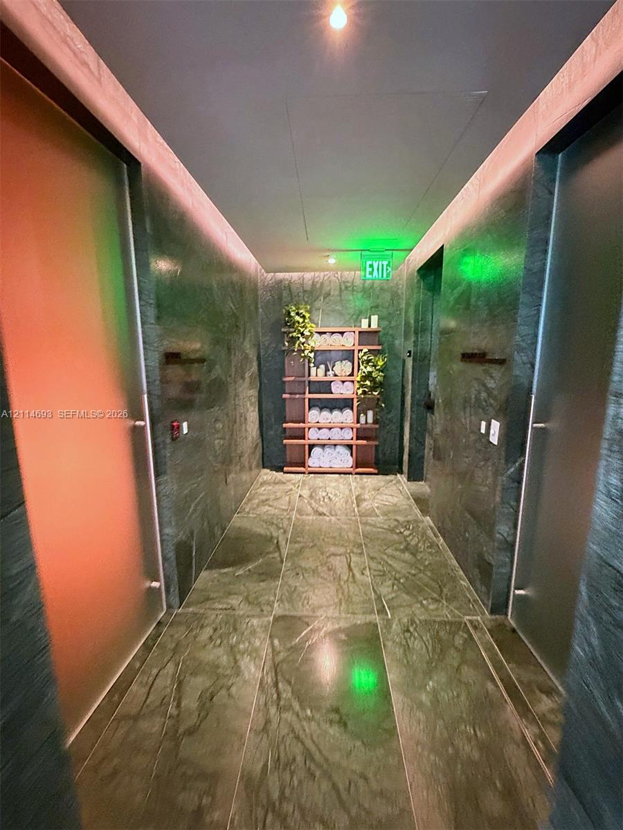 Hallway featuring full-height natural stone wall cladding, large-format stone floor tiles, recessed ceiling lighting, and built-in wood shelving