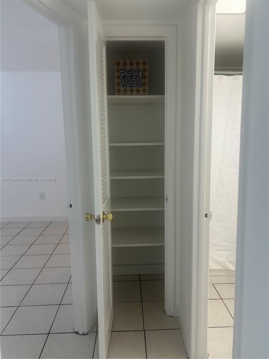 Built-in storage closet featuring louvered door, multiple shelves, and ceramic tile flooring