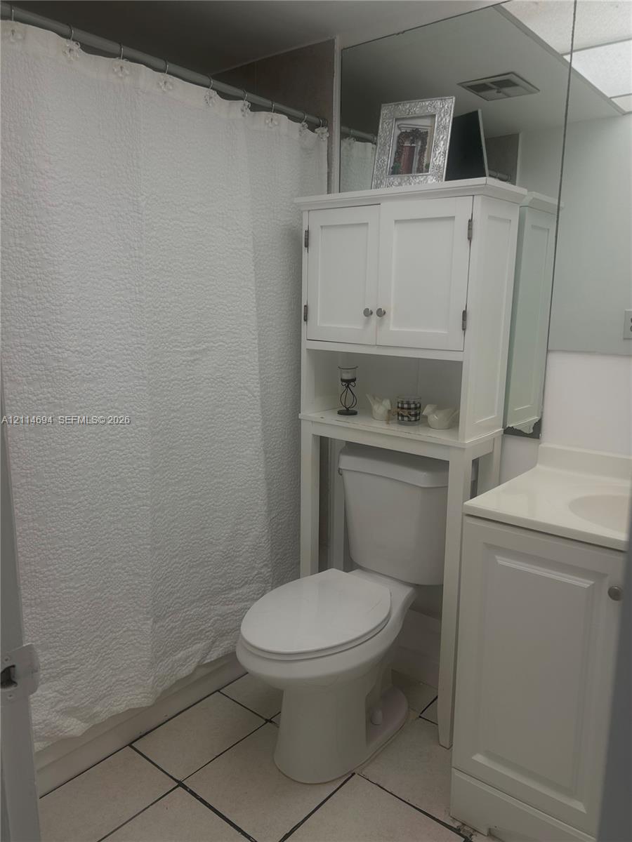 Bathroom featuring light-toned tile flooring, built-in white cabinetry, and a full-width vanity mirror