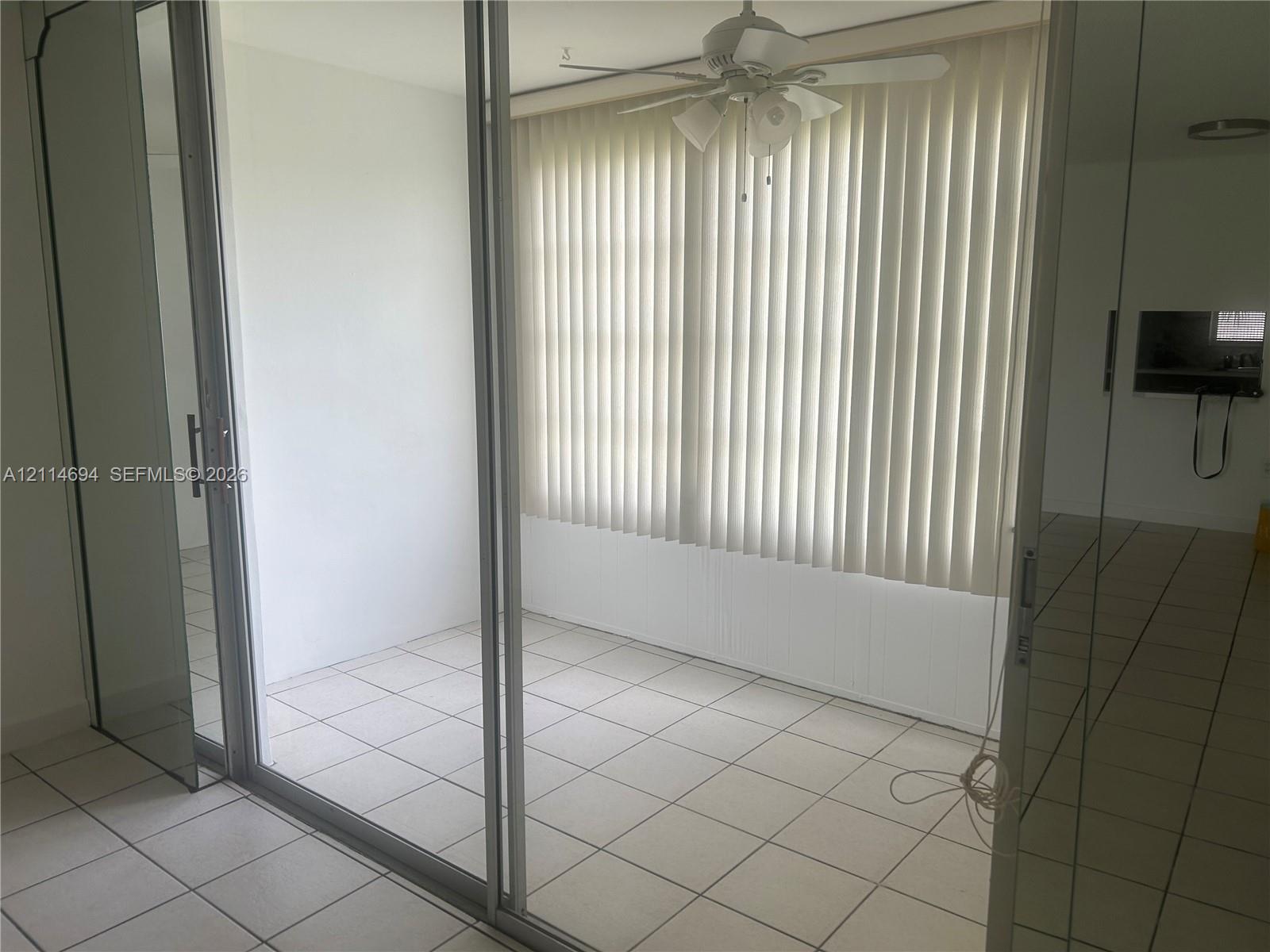Enclosed space with large-format tile flooring, sliding glass door entry, vertical window blinds, and a white ceiling fan with integrated light fixture