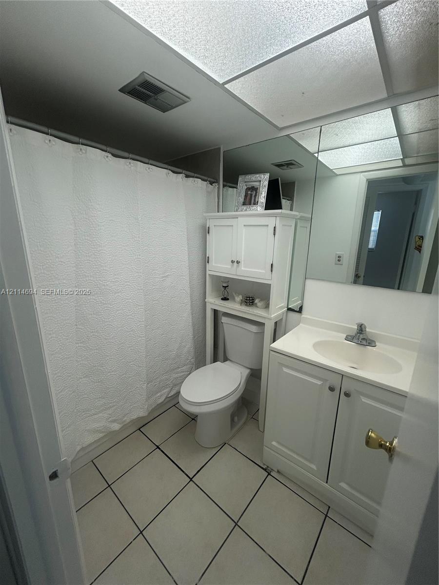 Bathroom featuring a vanity with an integrated countertop sink, full-width mirror, three-light fixture, and geometric patterned floor tiling