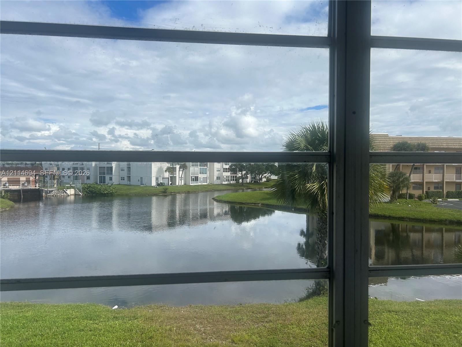 Waterfront exposure featuring a serene pond, manicured turf, and mature palm trees
