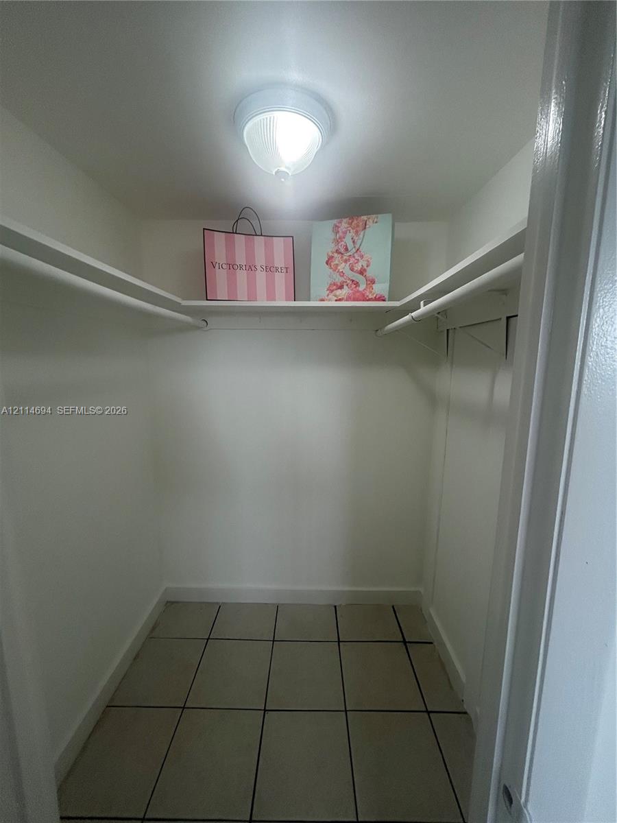 Storage closet featuring ceramic tile flooring, built-in shelving, dual hanging rods, and a ceiling-mounted light fixture