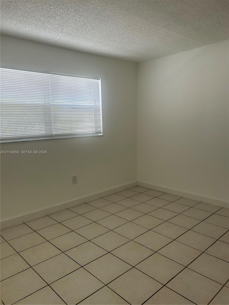 Neutral-toned ceramic tile flooring, solid white wall finishes, and a window with horizontal blinds