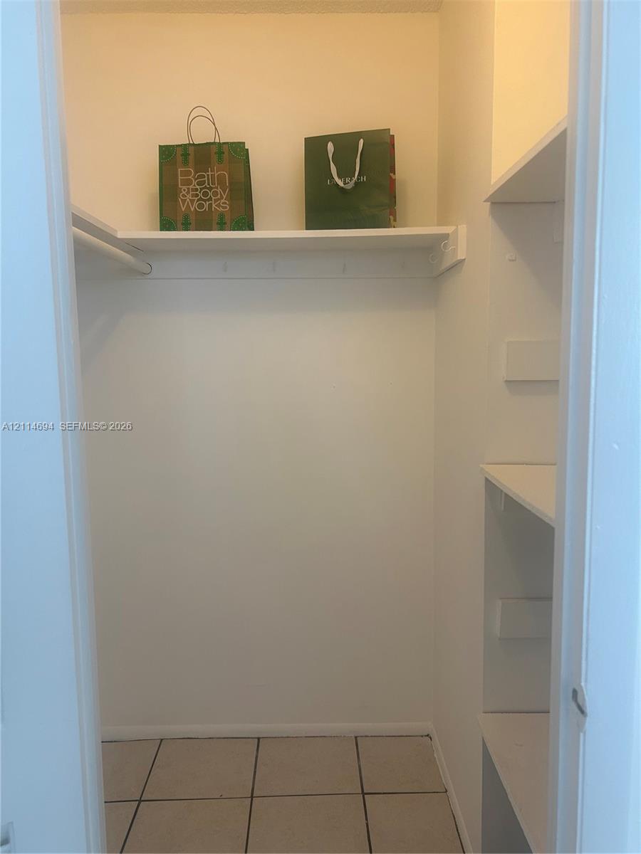 Storage closet featuring tile flooring, built-in shelving, and a hanging rod
