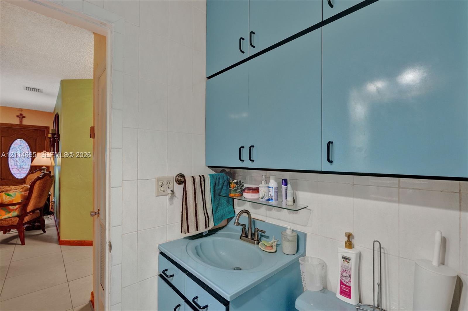 Built-in cabinetry with matte black hardware, integrated vanity sink, ceramic wall tiling, and glass shelving