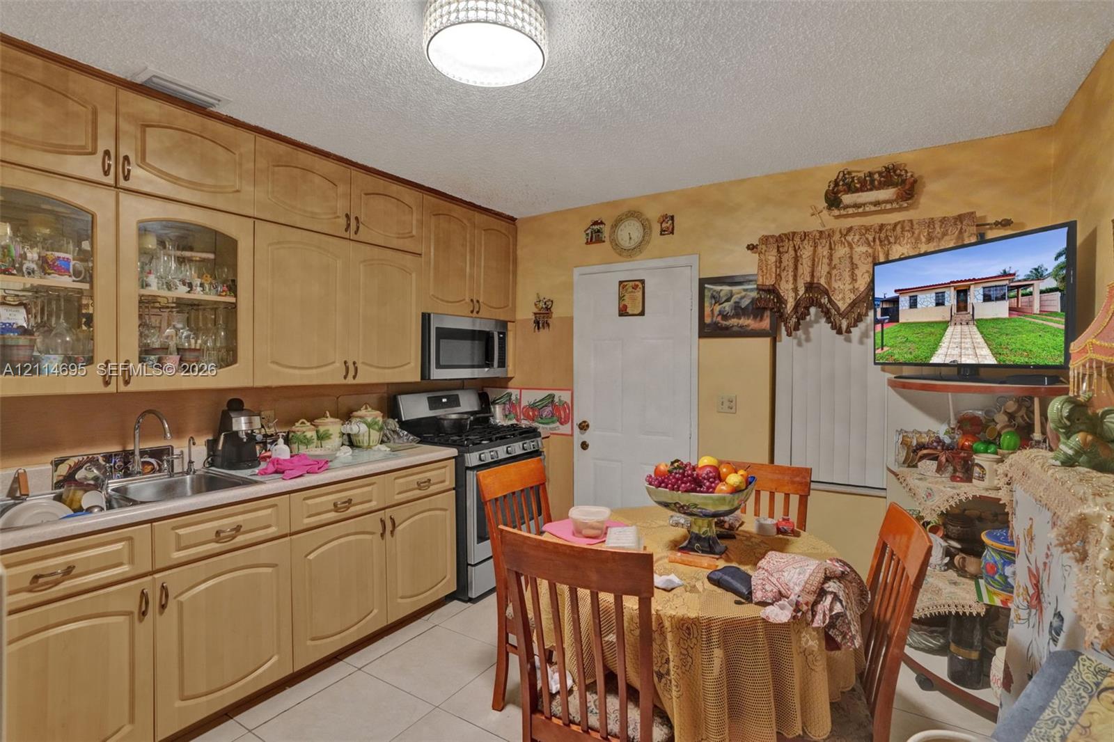 Kitchen featuring wood cabinetry with glass-panel upper doors, tile flooring, stainless steel sink with gooseneck faucet, and stainless steel microwave and range