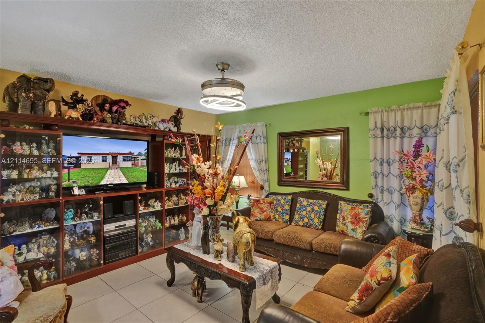 Living area featuring large-format ceramic tile flooring, built-in floor-to-ceiling cabinetry, a modern drum-style ceiling fan with integrated LED lighting, and a framed wall mirror
