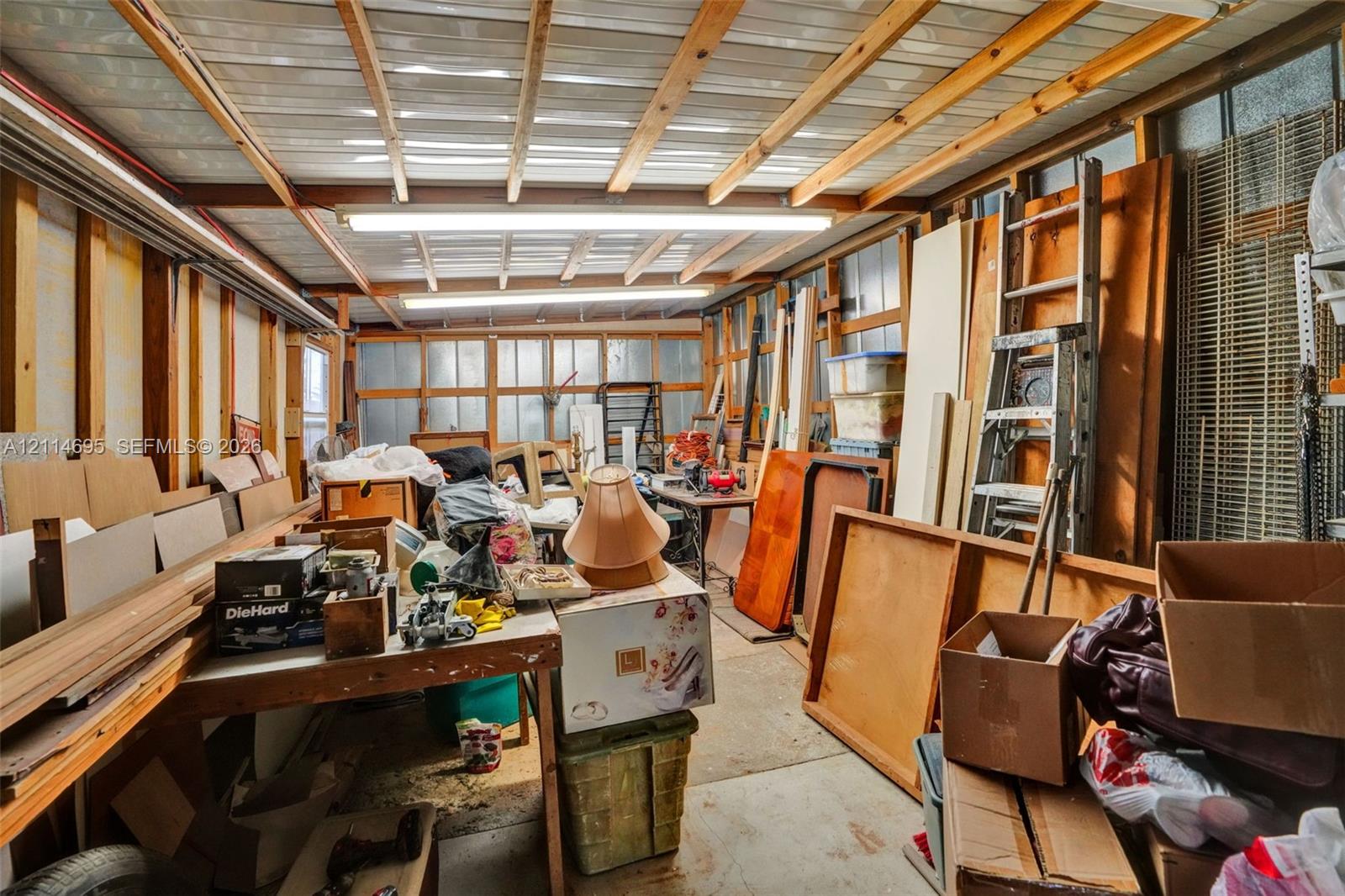 Enclosed structure featuring exposed wood framing, metal panel roofing, and overhead fluorescent lighting