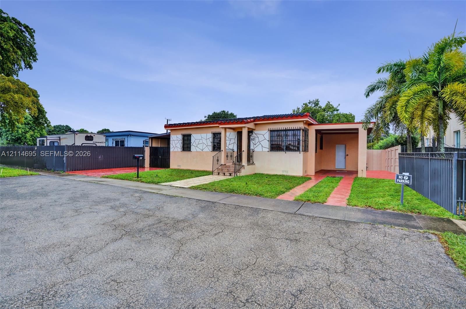 Single-story exterior featuring a decorative stone facade, attached carport, metal security window bars, and perimeter privacy fencing