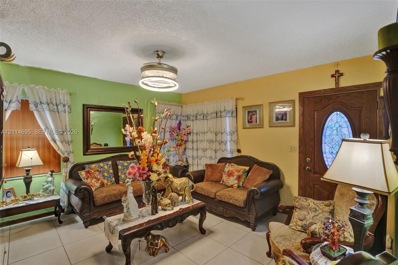 Living area featuring large format ceramic tile flooring, a modern circular LED flush-mount ceiling fan, and a wood entry door with an oval decorative glass insert
