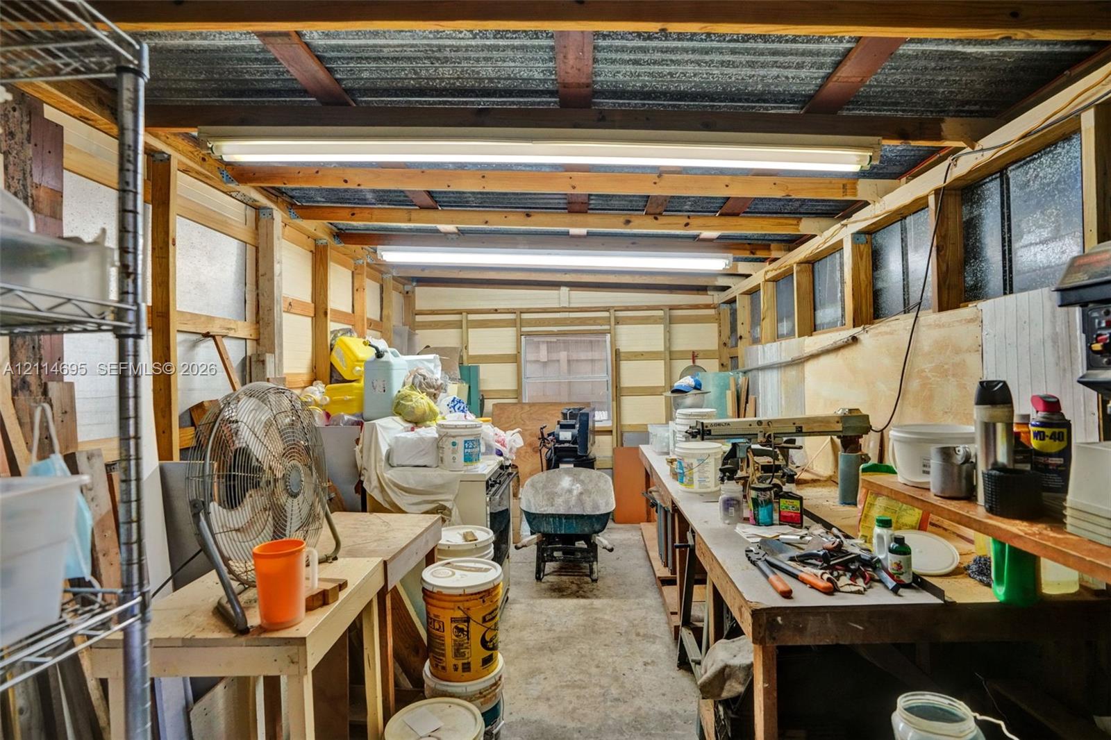 Workshop space featuring exposed timber framing, concrete flooring, corrugated metal ceiling panels, and integrated overhead fluorescent lighting