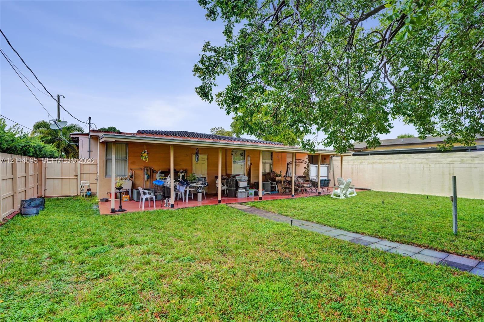Backyard featuring a covered concrete patio, enclosed wood fencing, masonry perimeter wall, stone paver pathway, and mature tree canopy