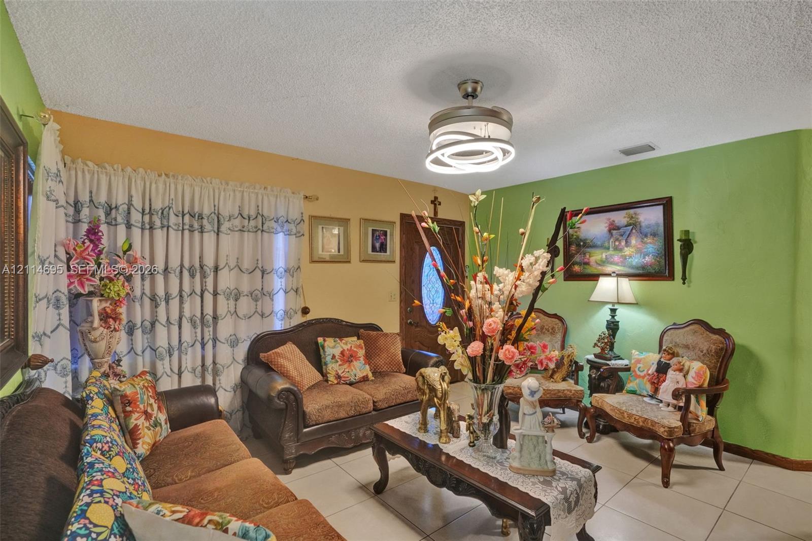 Living area featuring large format tile flooring, modern circular LED flush-mount ceiling light with integrated fan, and solid wood entry door with oval glass insert