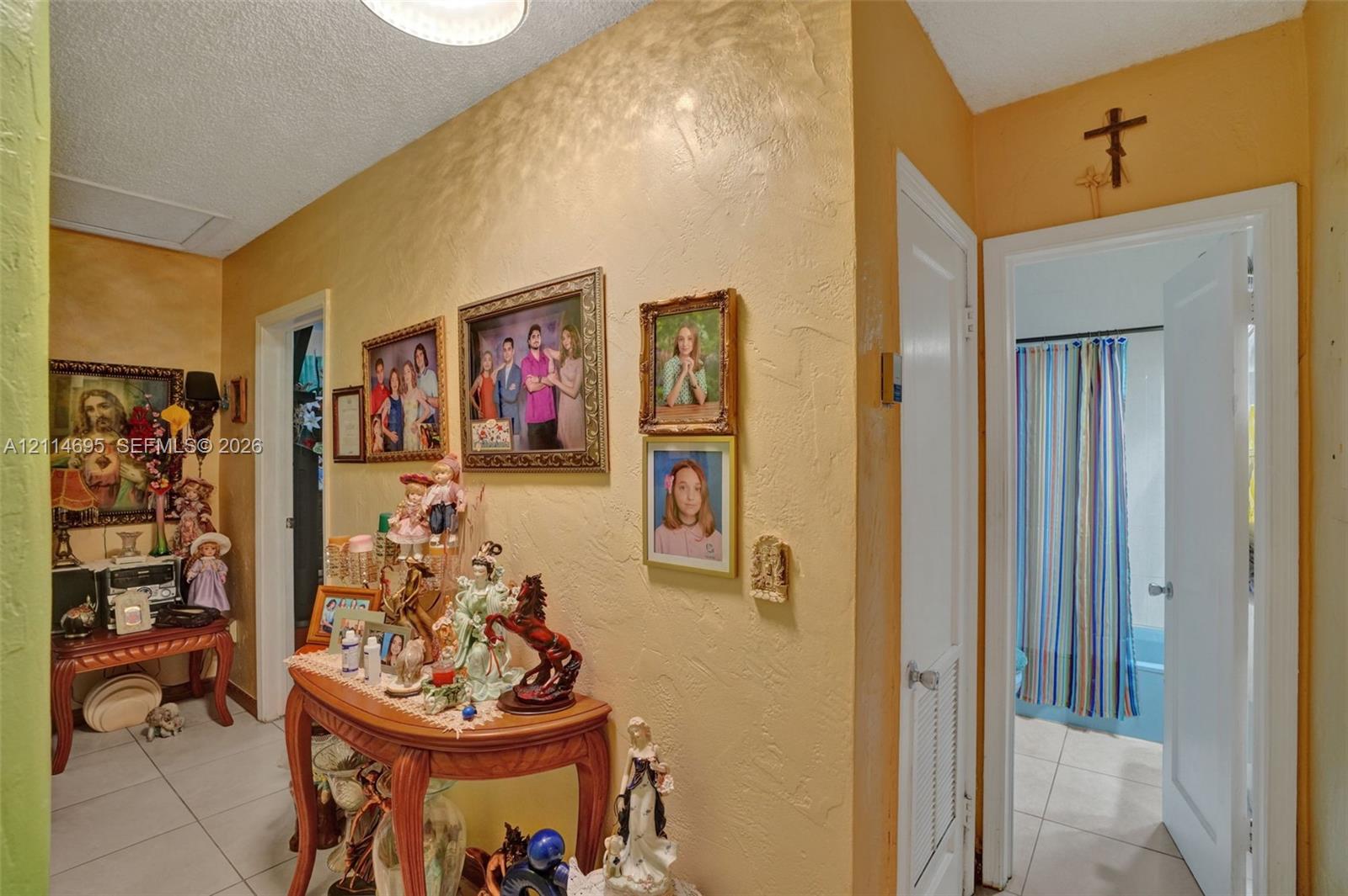 Interior hallway featuring textured wall finishes, tile flooring, and a dedicated utility closet with louvered doors