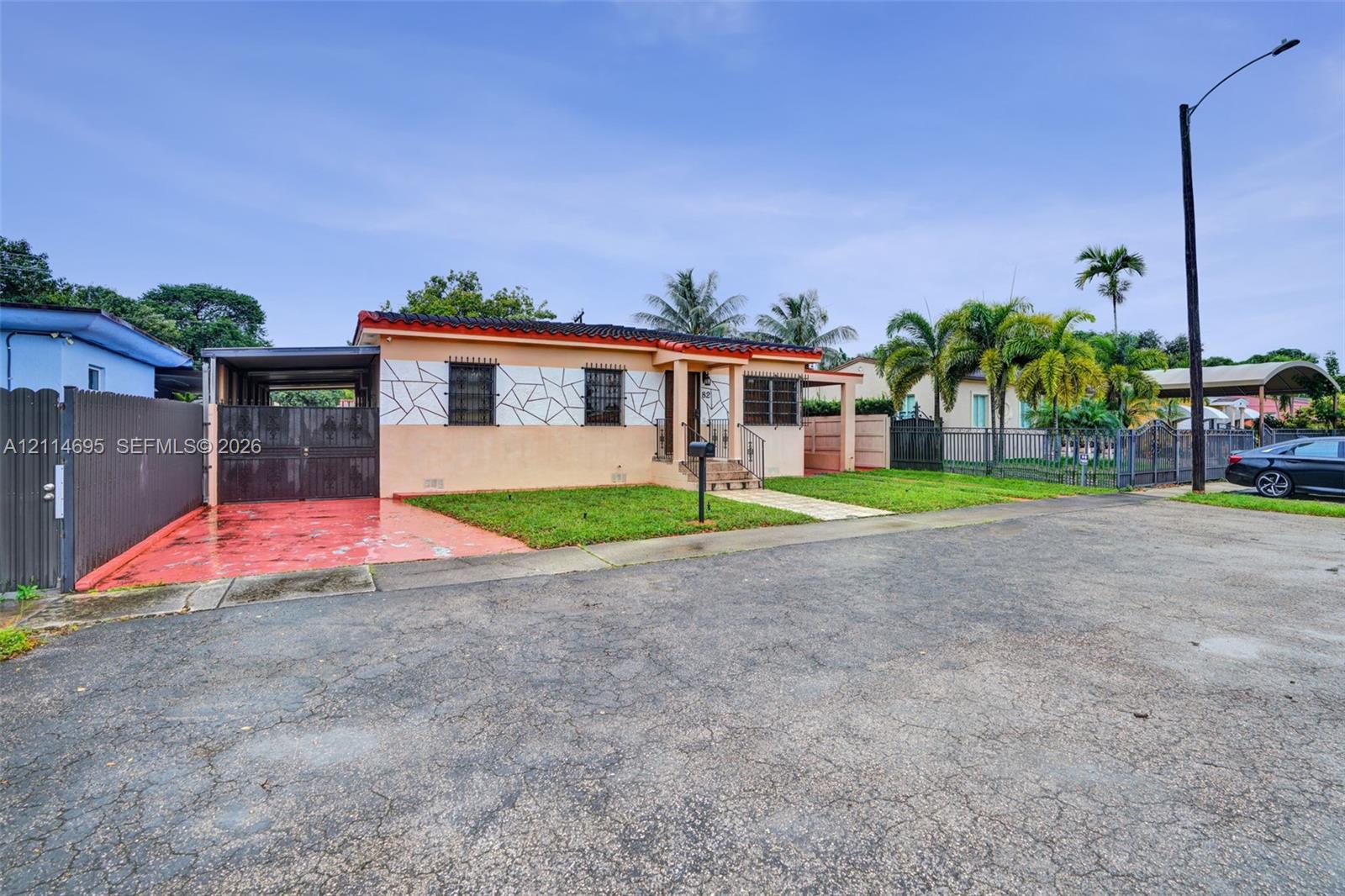 Single-story residence featuring a decorative geometric exterior facade, a covered carport, metal window security grates, and exterior masonry fencing