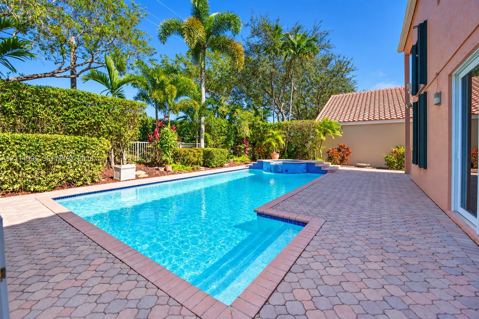 In-ground swimming pool with a raised spillover spa, expansive paver patio, and privacy hedges