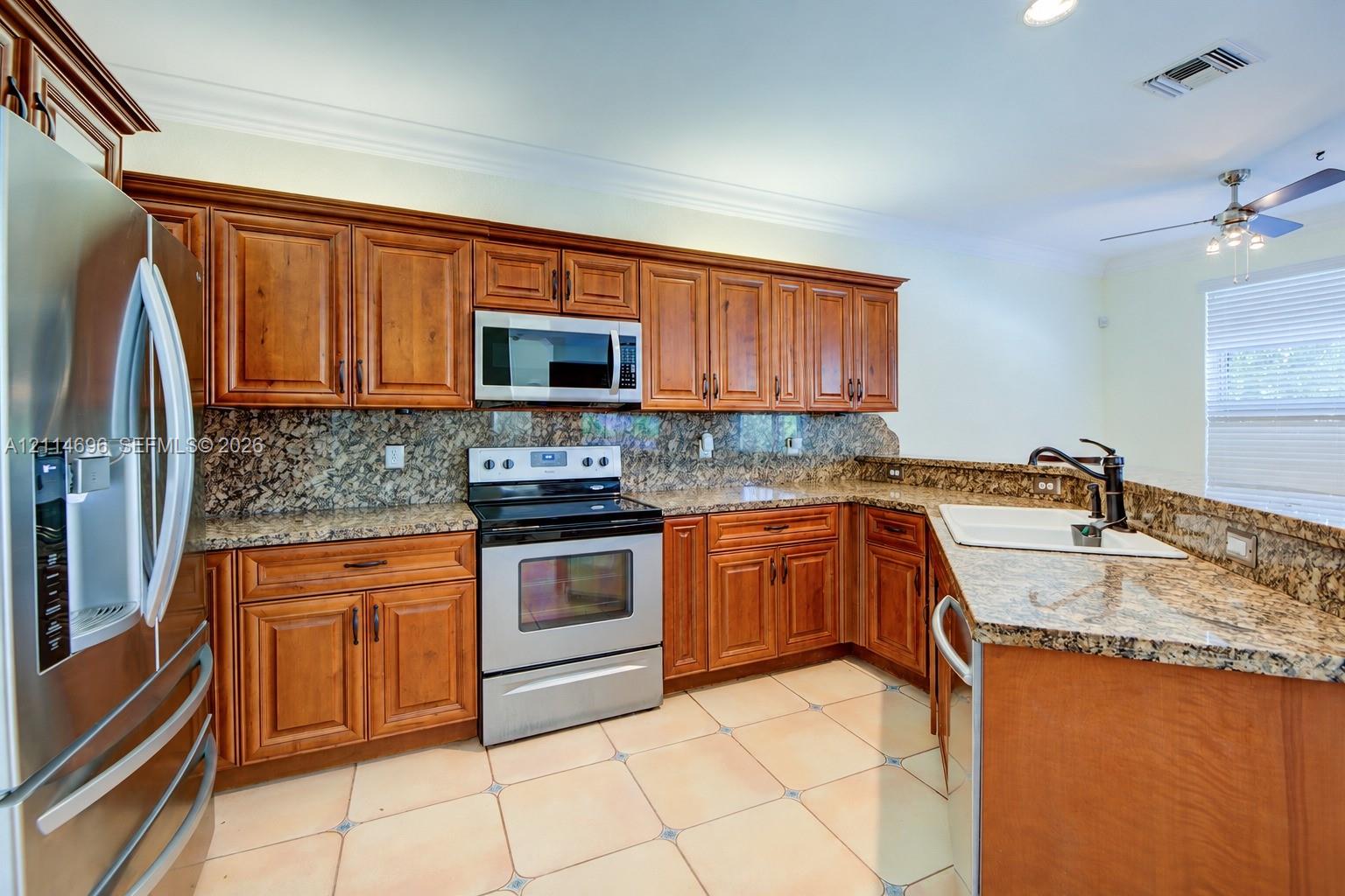 Kitchen featuring raised-panel wood cabinetry, granite countertops and backsplash, stainless steel appliances and tile flooring