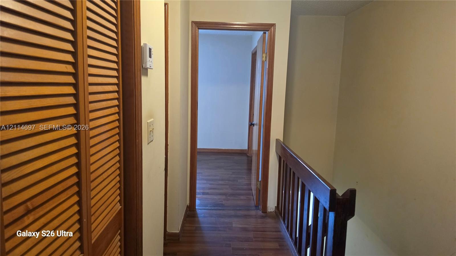 Hallway featuring wood-finish flooring, wood-toned louvered closet doors, and a wood-railing staircase balustrade