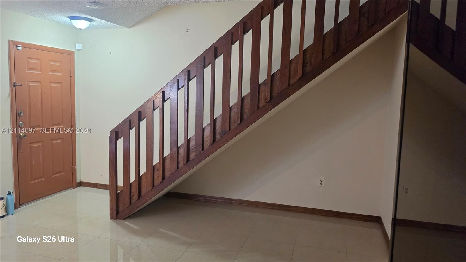 Entrance featuring a solid-core door, high-gloss tile flooring, and a wood-slat staircase railing