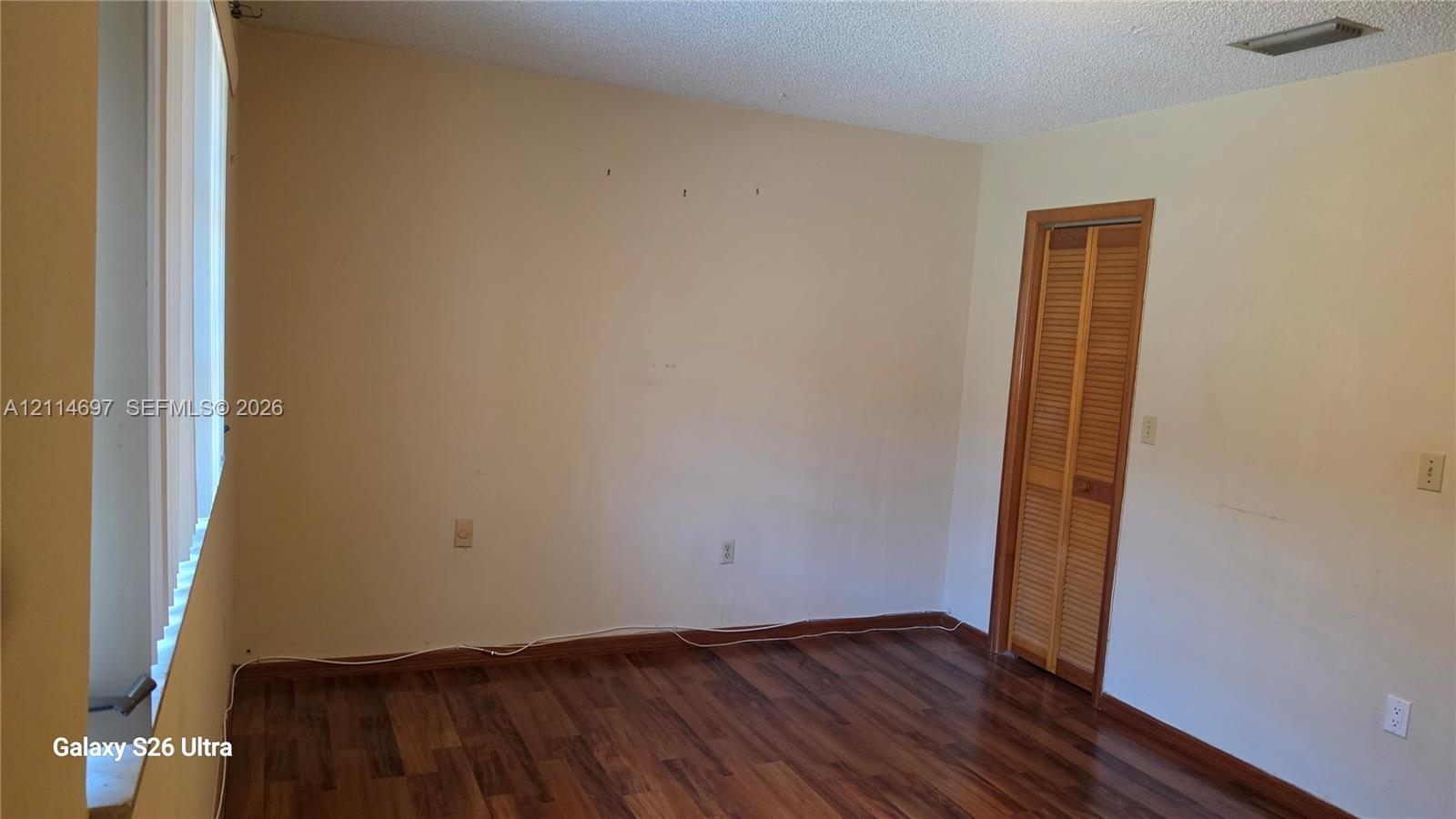 Interior room featuring wood-finish flooring, vertical slat window blinds, and a built-in closet with louvered doors
