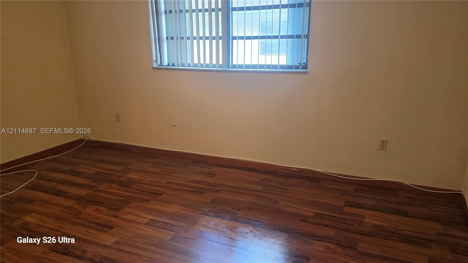 Room featuring wood-finish flooring and a window with vertical blinds