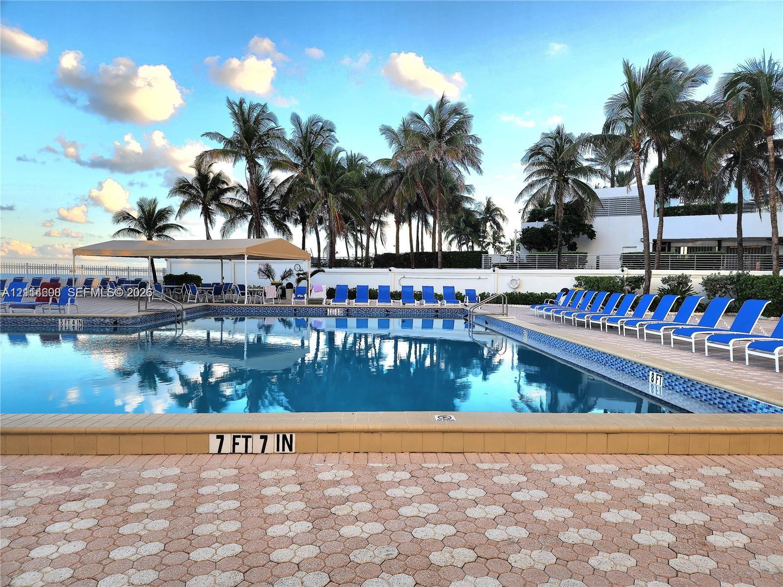 Swimming pool featuring mosaic tile trim, a tan stone-finish pool deck, and a shaded pavilion