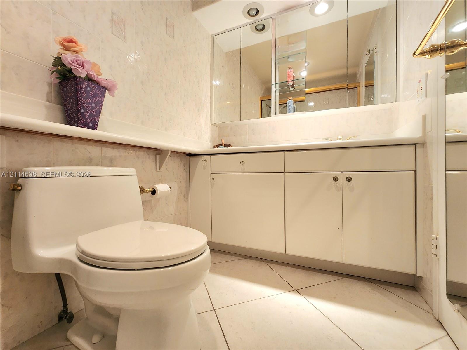 Bathroom vanity featuring white cabinetry, a solid-surface countertop, and an integrated tri-fold medicine cabinet with recessed lighting