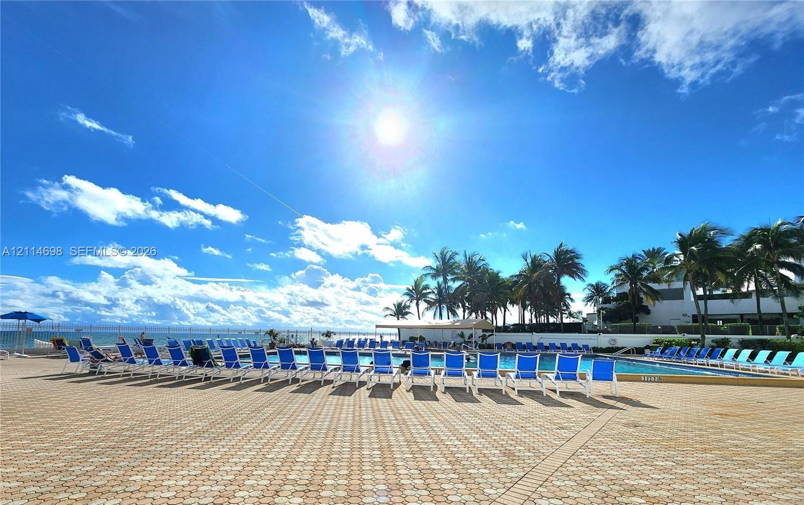 Swimming pool featuring a paved pool deck, perimeter fencing, and mature palm trees