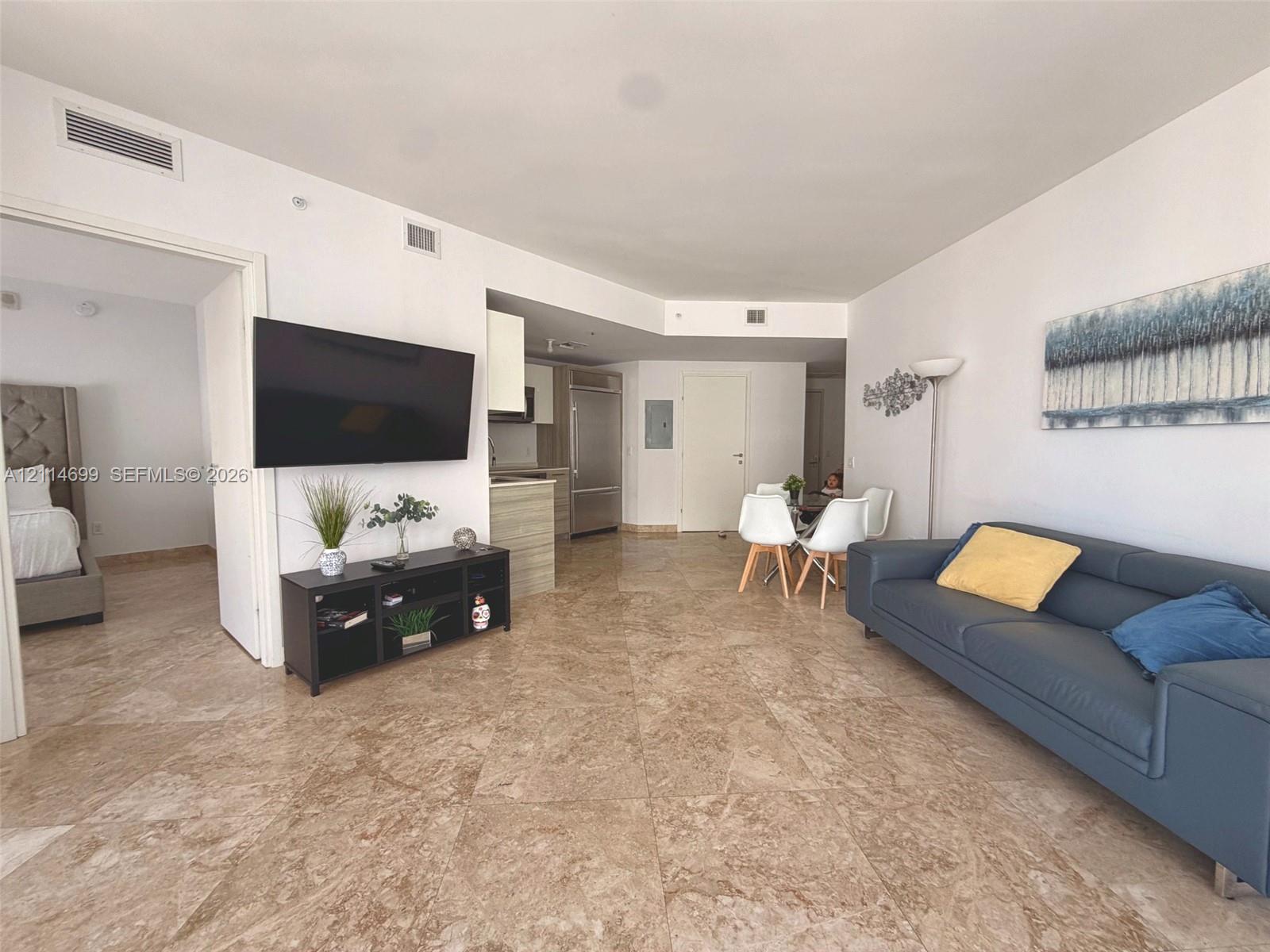 Open-concept interior featuring large-format stone tile flooring, high ceilings, built-in stainless steel refrigerator, and recessed lighting