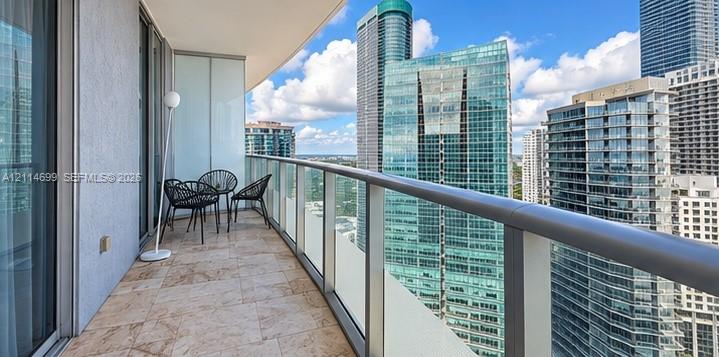 Private balcony featuring stone tile flooring and a glass panel railing