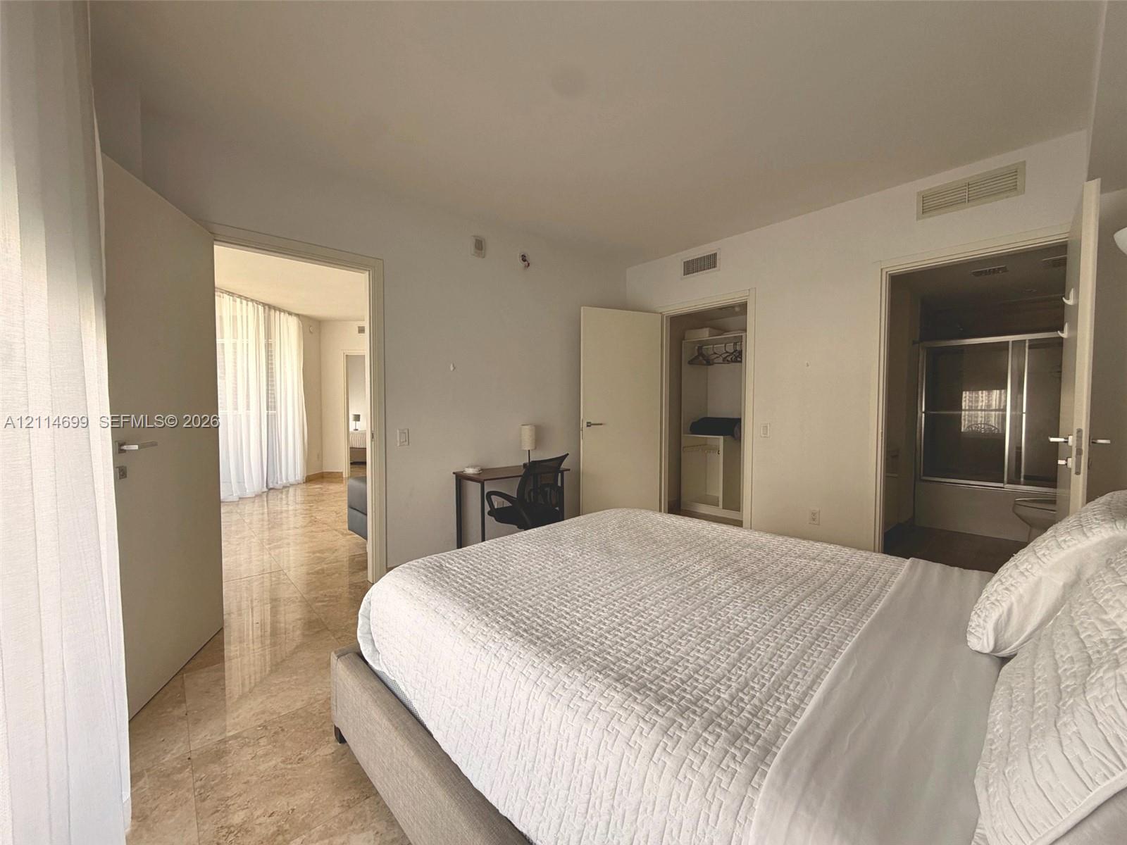 Spacious room featuring polished stone flooring, built-in closet cabinetry, and a private ensuite bathroom with a glass-enclosed shower